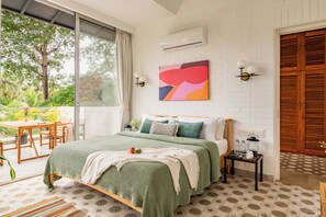 Een slaapkamer met een groot bed, uitzicht op groen, een witte bakstenen muur en een houten deur.