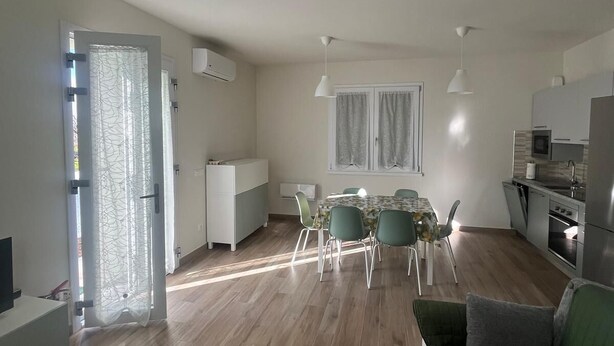 En moderne stue med en grøn sofa, et spiseområde med bord og stole, samt et køkken med køleskab og komfur.