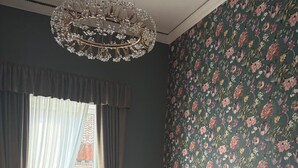 A bedroom with a large bed, floral wallpaper, a chandelier, and a view of a building outside. - Zapata Relais (Naples)