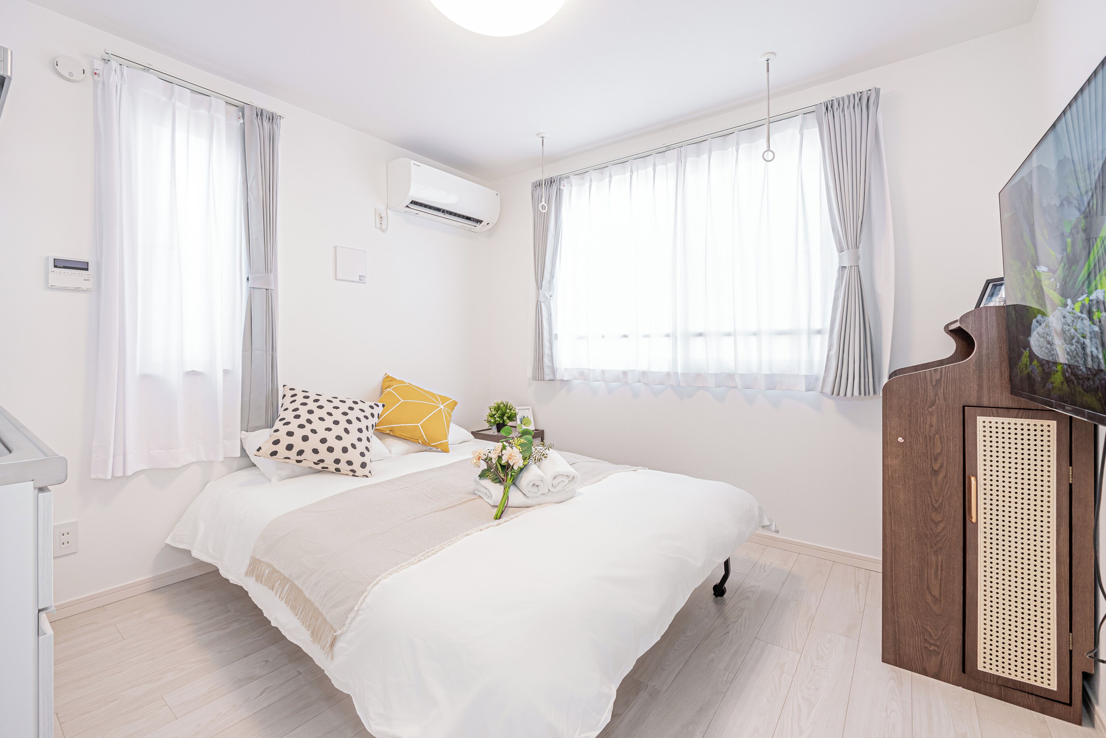 A bedroom with a bed, curtains, an air conditioning unit, a wooden cabinet, and a painting on the wall.