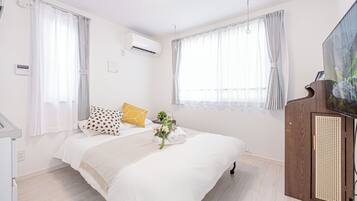 A bedroom with a bed, curtains, an air conditioning unit, a wooden cabinet, and a painting on the wall.