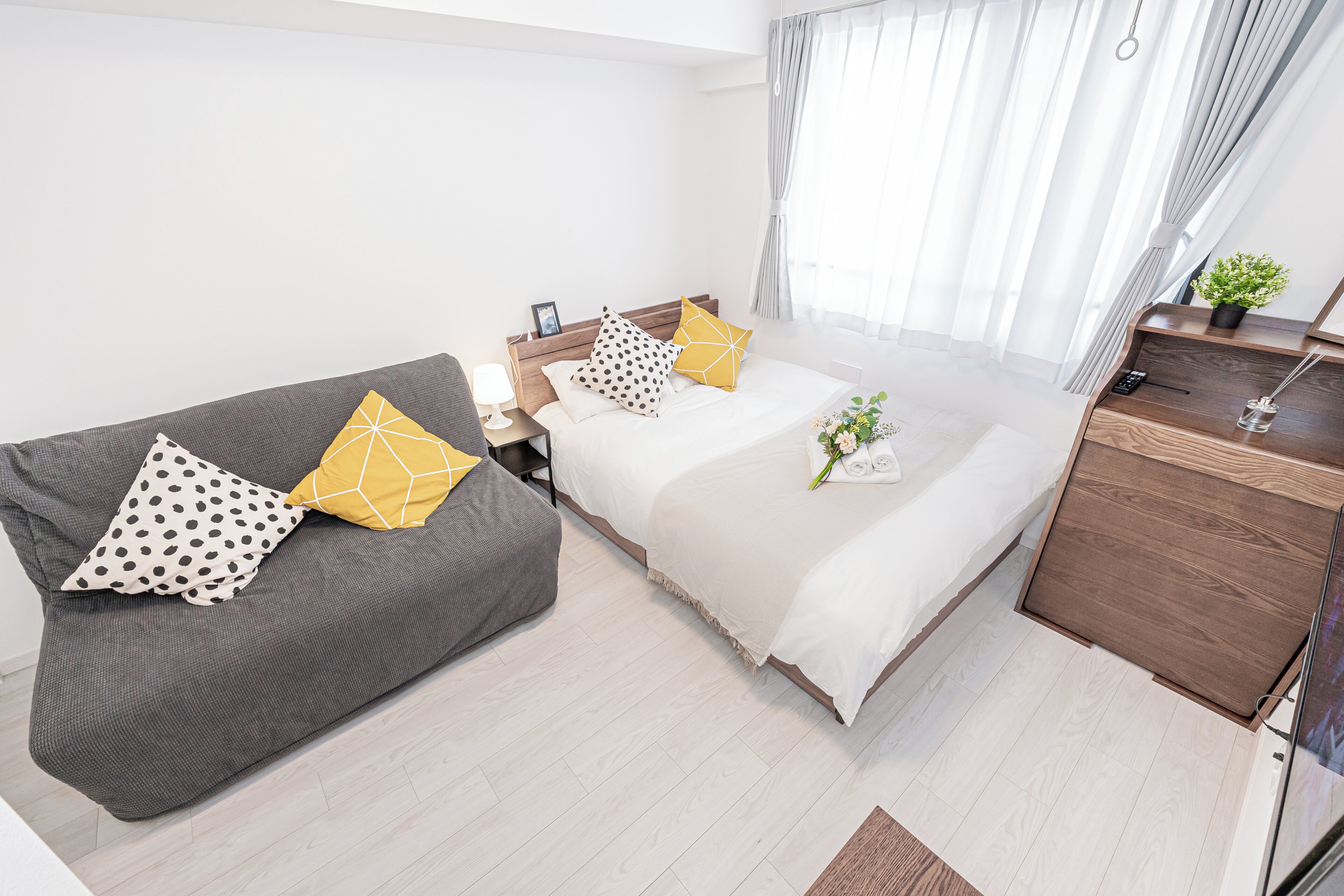 A modern bedroom with a bed, a sofa, a bedside table, and a dresser.