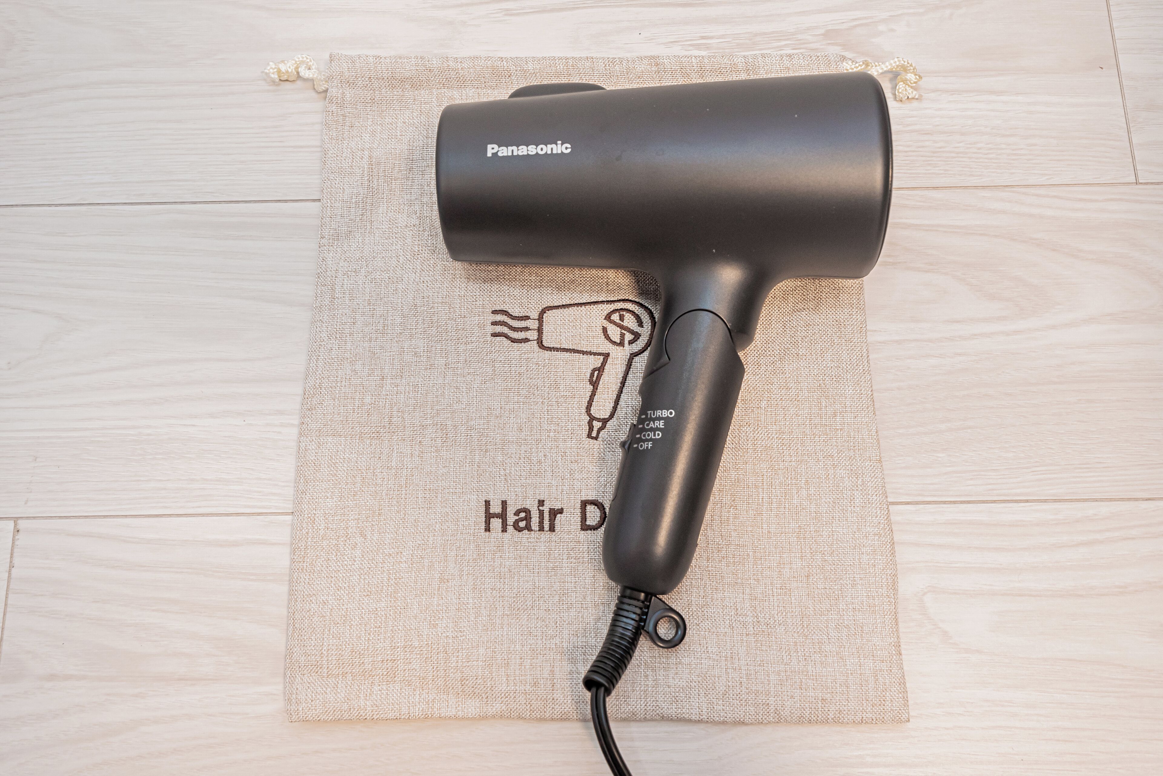 Un secador de pelo Panasonic sobre un paño color beige con un dibujo de una mano sosteniendo un secador de pelo y el texto 'Hair Dryer'.