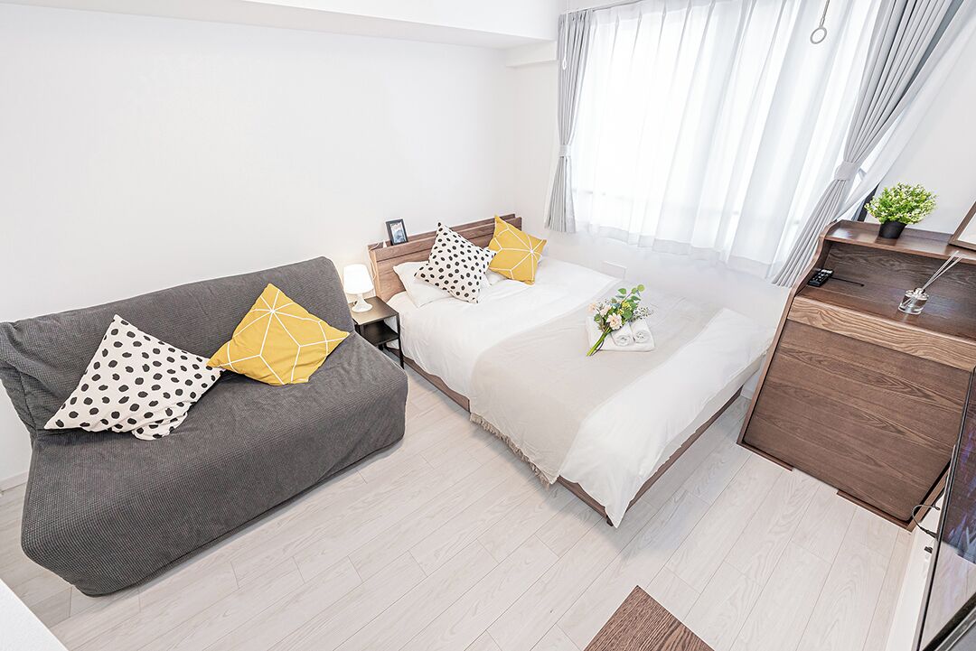 A modern bedroom with a bed, a sofa, a bedside table, and a dresser.