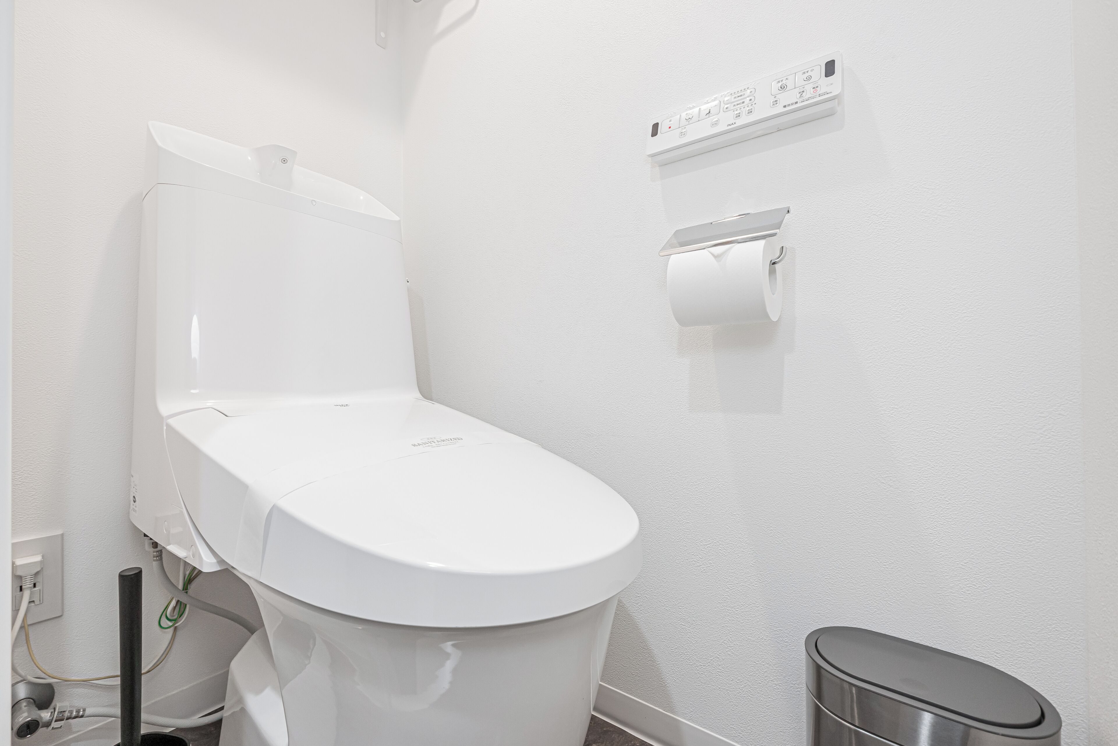 Eine weiße Toilette mit Spülhebel, Papierhandtuchspender und Mülleimer.