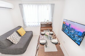 A modern living room with a sofa, dining table set, and a cityscape TV. - Shinjuku16 (Shinjuku-ku)
