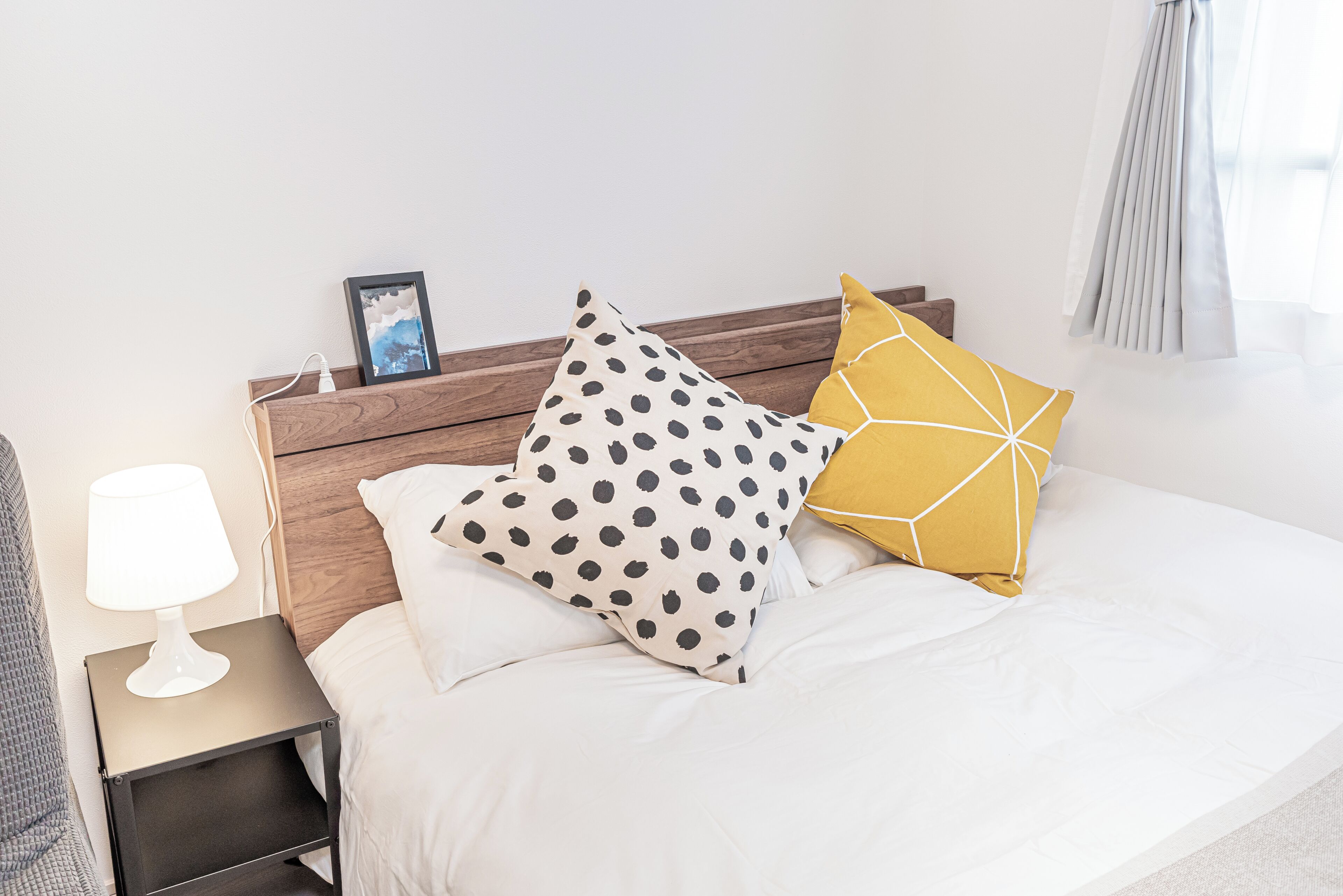 A neatly made bed with white bedding, a wooden headboard, and two decorative pillows.