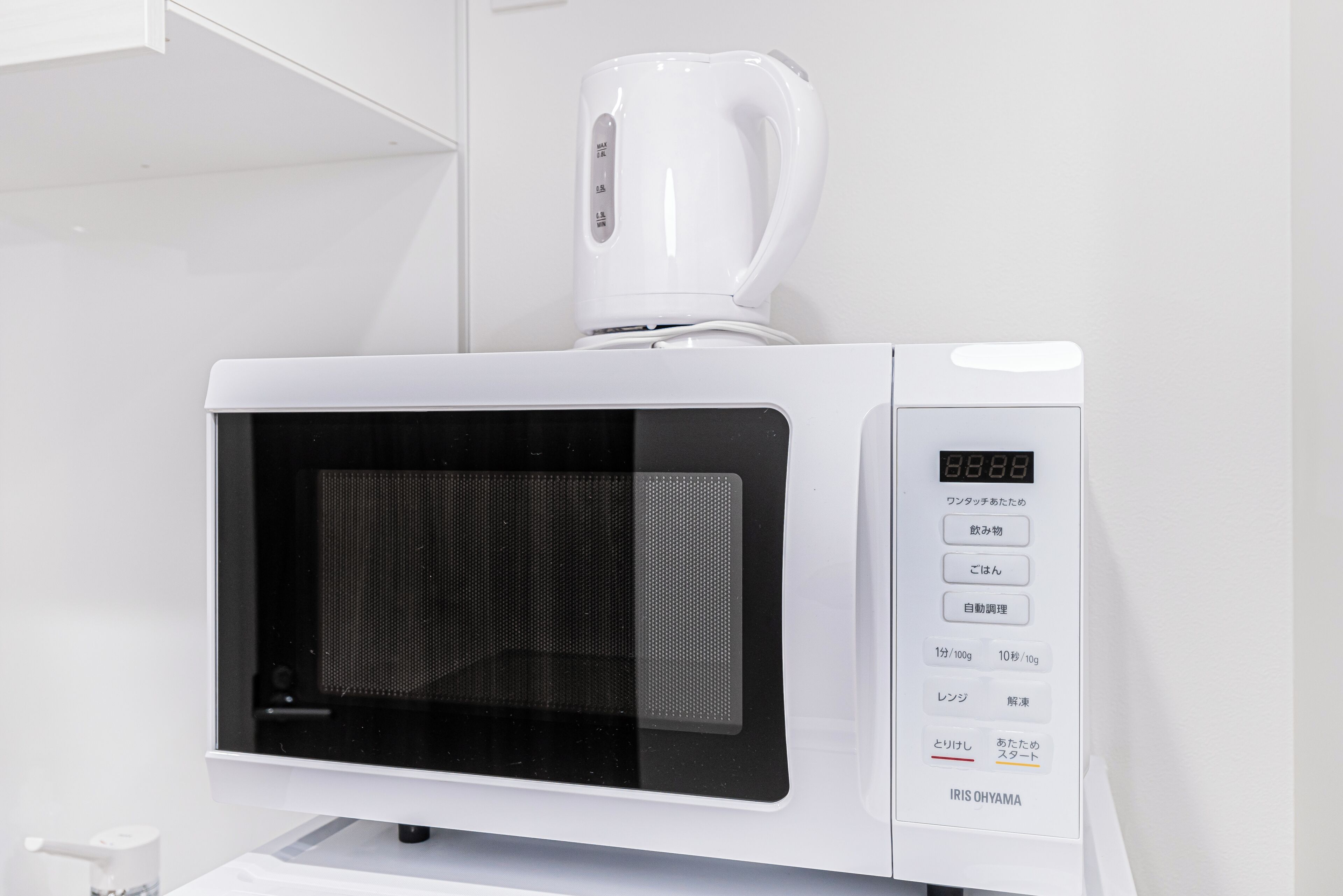A white microwave with a digital display and a coffee maker on top.