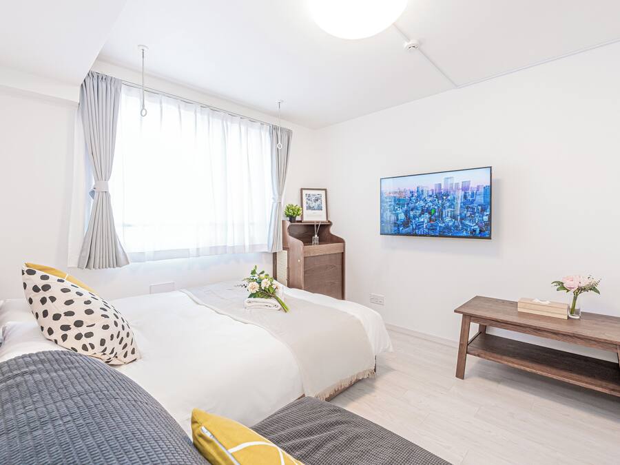A modern hotel room with a large bed, a bedside table with a lamp, a cityscape painting on the wall, and a small wooden bench.