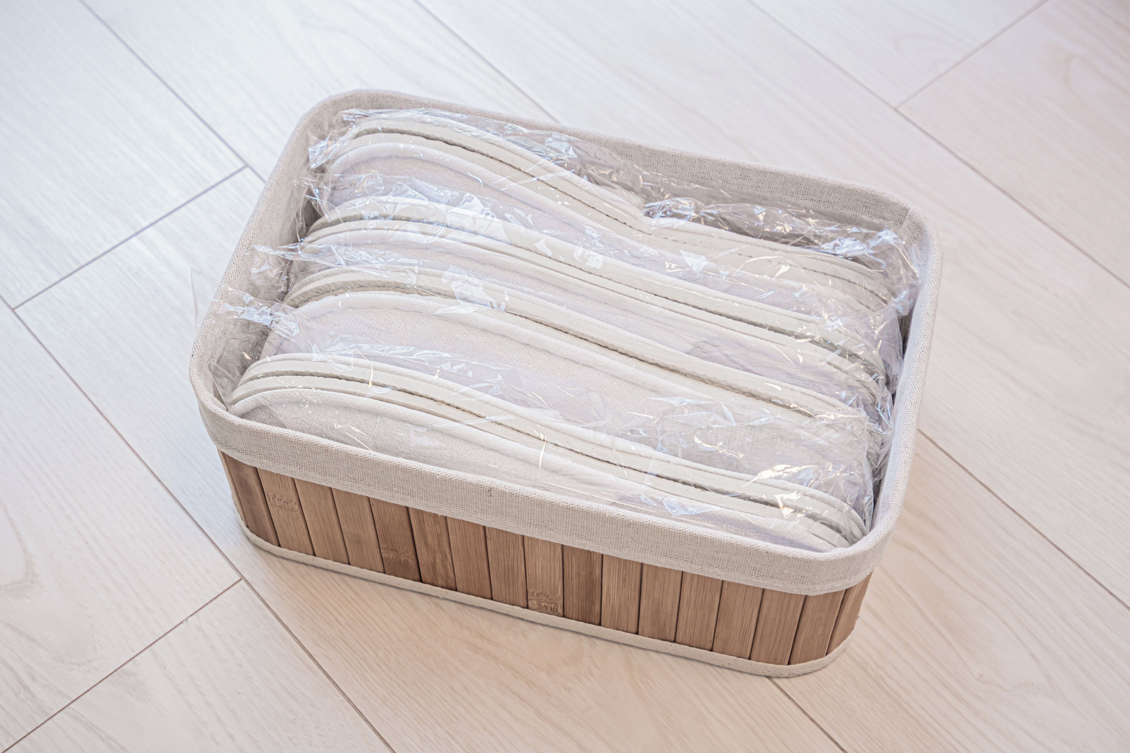 A rectangular storage bin with a woven exterior and a fabric interior, placed on a wooden floor.
