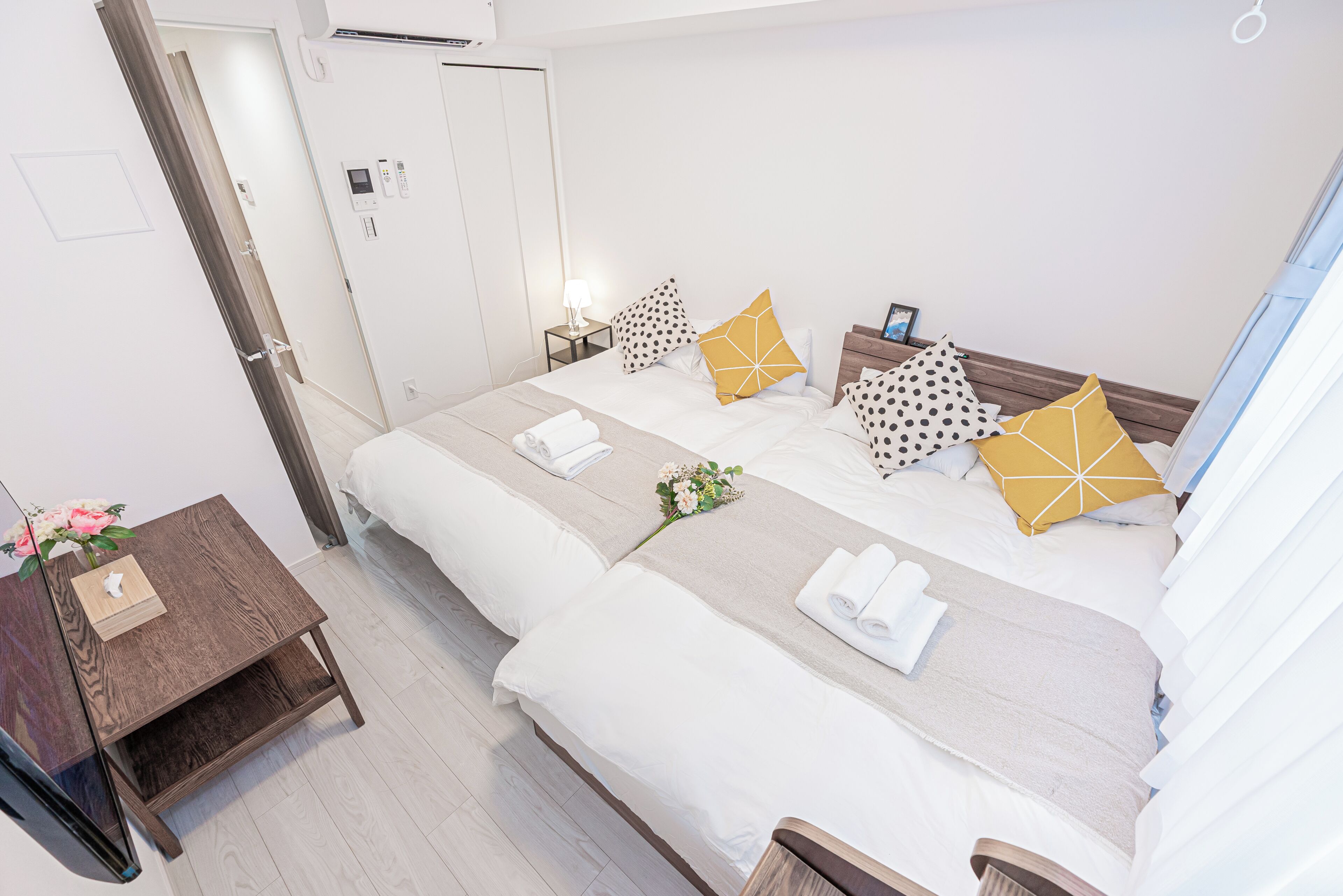 A hotel room with two beds, a bedside table with a lamp, a nightstand with a phone, and a wall-mounted air conditioner.