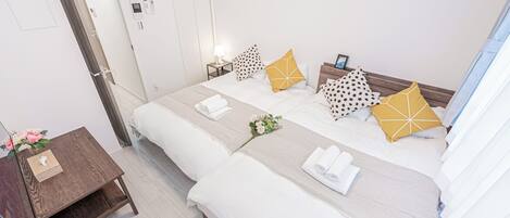 A hotel room with two beds, a bedside table with a lamp, a nightstand with a phone, and a wall-mounted air conditioner.