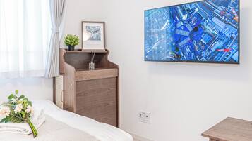 A hotel room with a bed, a wooden nightstand, a framed picture, a wall-mounted TV, and a window with curtains.