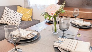 Una mesa de comedor dispuesta con platos, cubiertos y vasos, con un jarrón de flores en el centro.
