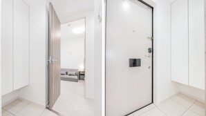 Una habitación de hotel moderna con una puerta corredera, un sofá gris, una mesita de noche y una lámpara.