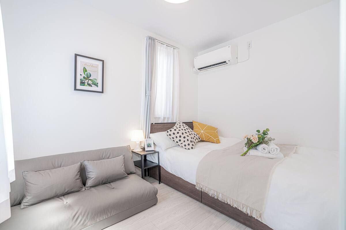 Una habitación de hotel con una cama, un sofá, una mesita de noche, un equipo de aire acondicionado y un cuadro en la pared.