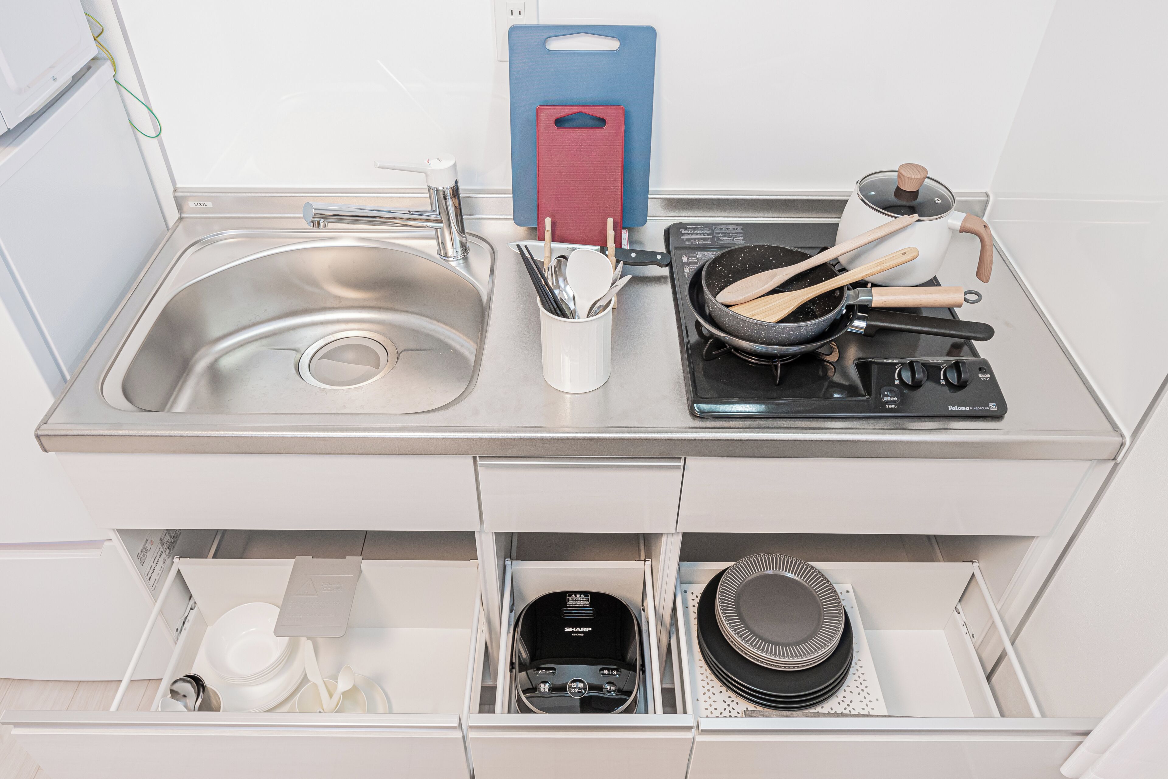 A kitchen with a stainless steel sink, a stove, and a drawer with kitchen utensils.