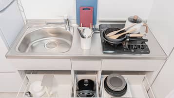 A kitchen with a stainless steel sink, a stove, and a drawer with kitchen utensils.