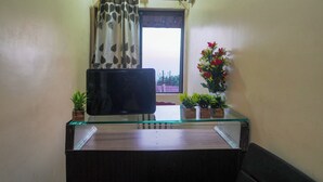 A room with a glass-top desk, a flat-screen TV, a potted plant, and a window with a curtain. - Hotel Shreekrupa Residency (Mahabaleshwar)