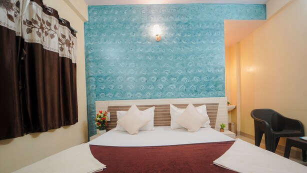A hotel room with a large bed, a nightstand, a small table, a chair, and a wall with a patterned design. - Hotel Shreekrupa Residency (Mahabaleshwar)
