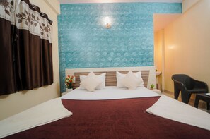 Een hotelkamer met een groot bed, een nachtkastje, een klein tafeltje, een stoel en een muur met een decoratief patroon.