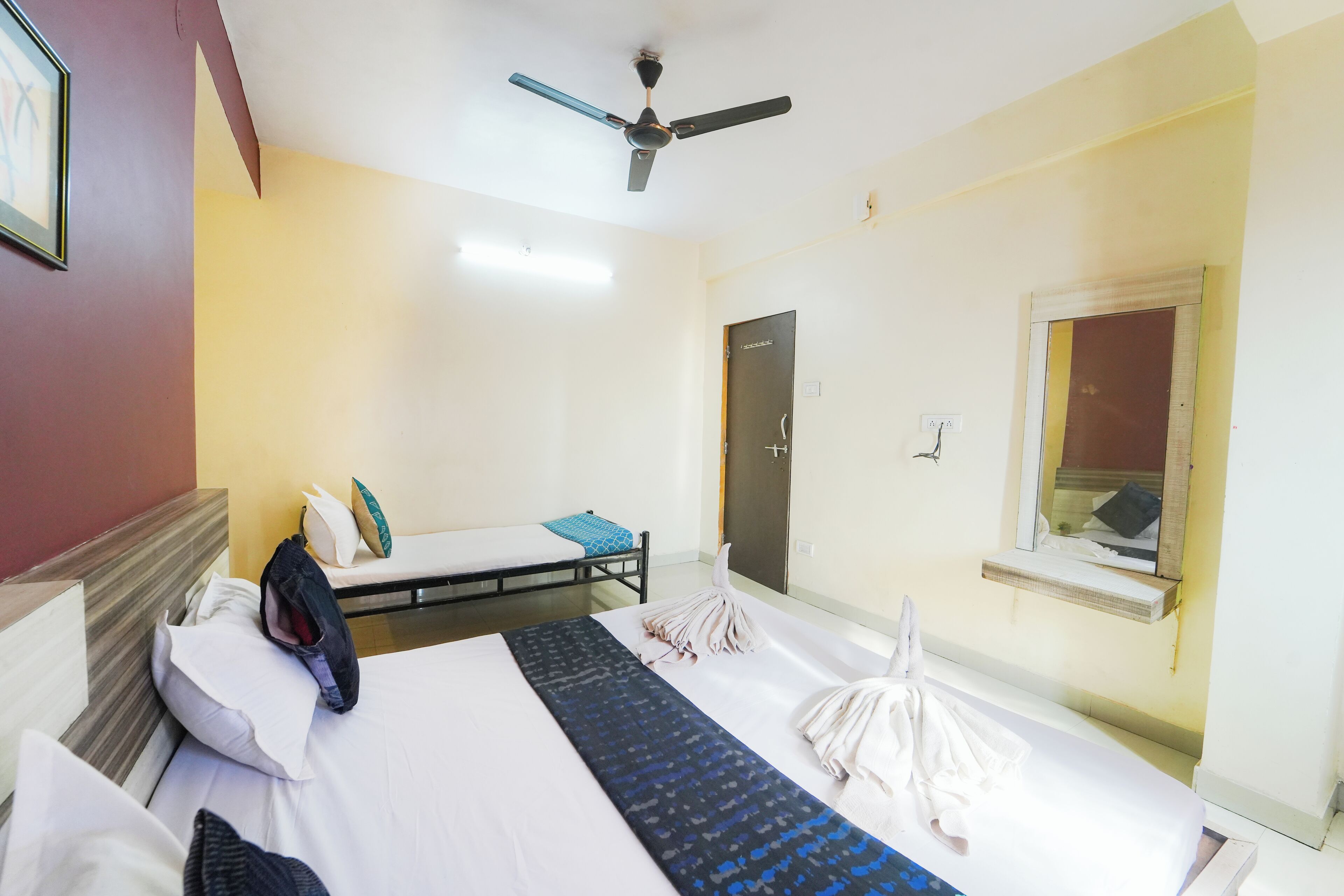 A hotel room with a bed, a desk, a ceiling fan, a window, and a door.
