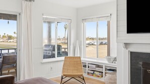 A room with a large window, a wicker chair, a bookshelf, and a fireplace. - Remodeled 4BR Bayfront Home | Sleeps 12 | Stunning Views + BBQ Patio (San Diego)