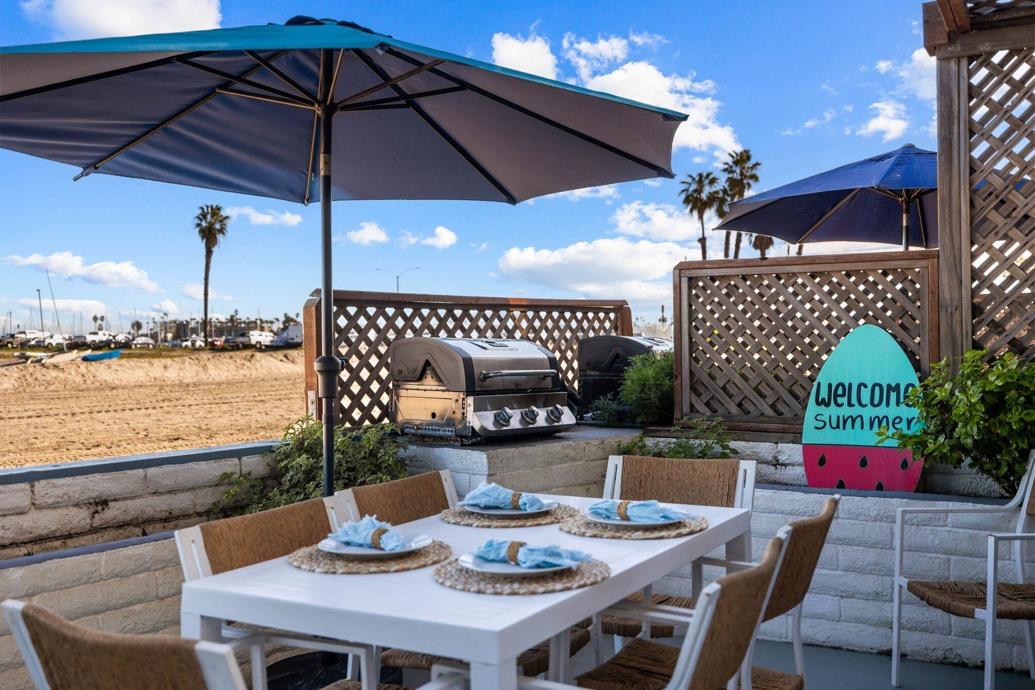 An outdoor patio with a table set for dining, a grill, and a welcome sign.