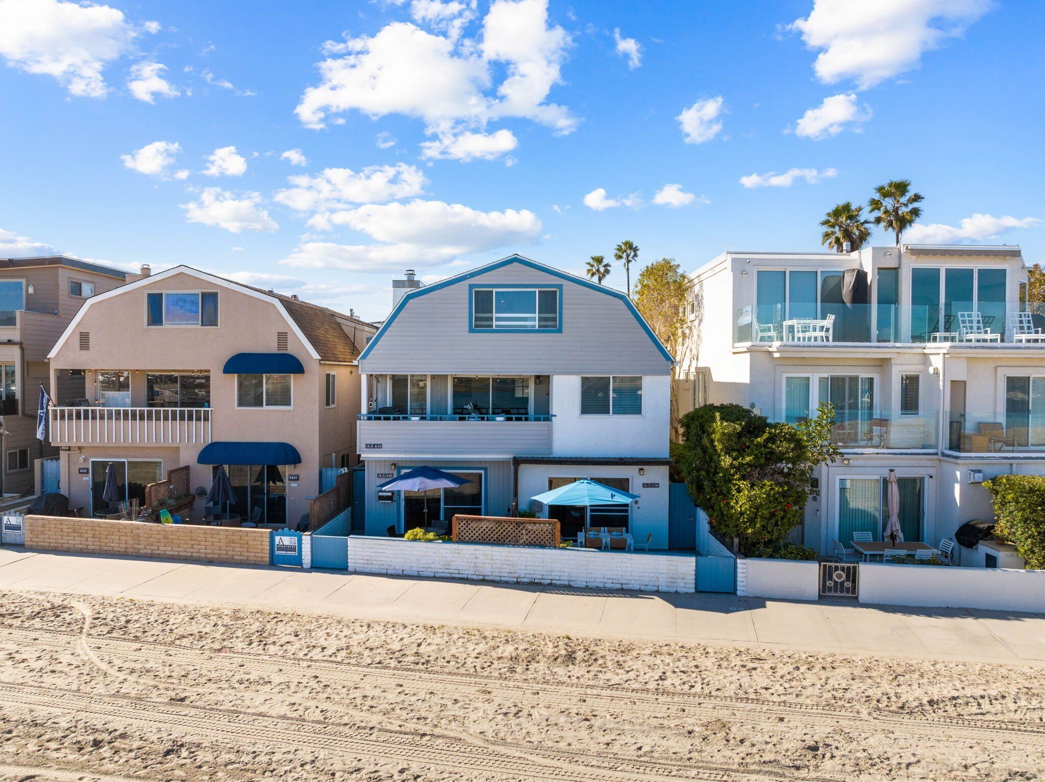 A beachfront property with a two-story house featuring a balcony, a covered patio, and a view of the ocean.