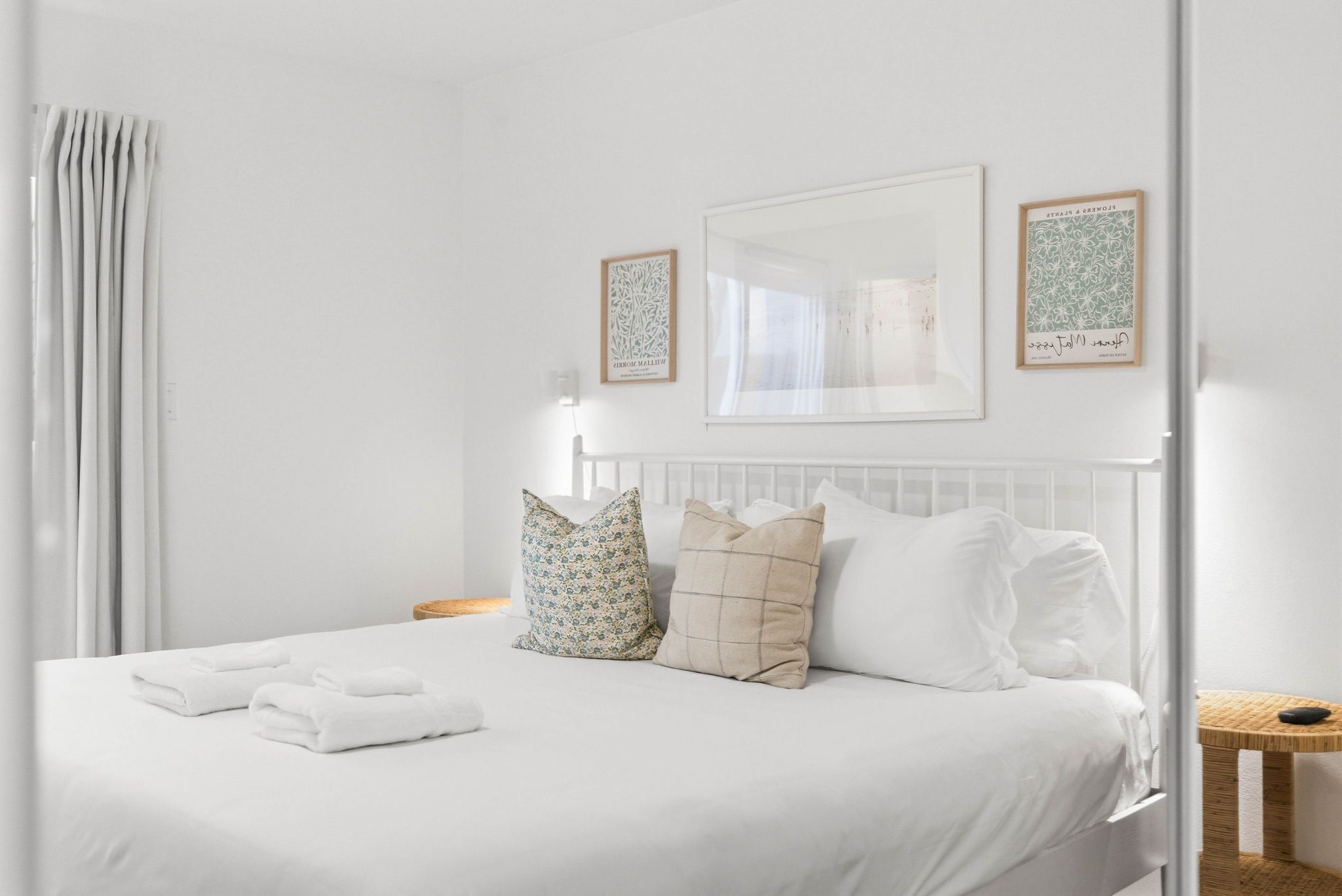 A neatly made bed with white linens, two pillows, and folded towels. There are two framed artworks on the wall above the bed.