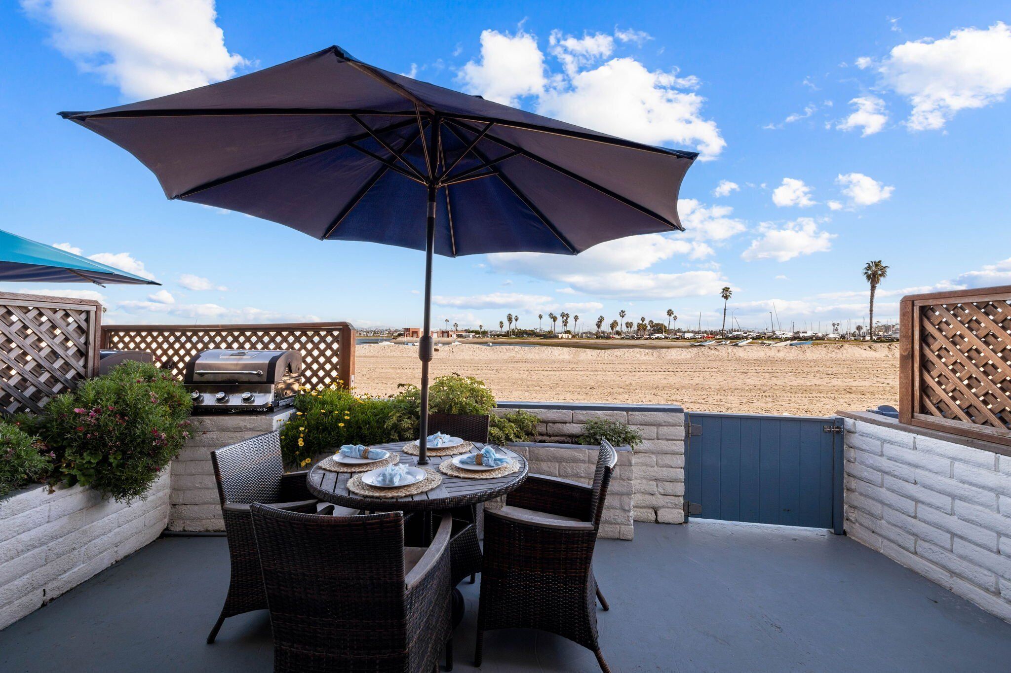 Une terrasse extérieure aménagée avec des meubles en osier, un barbecue et une vue sur la plage.