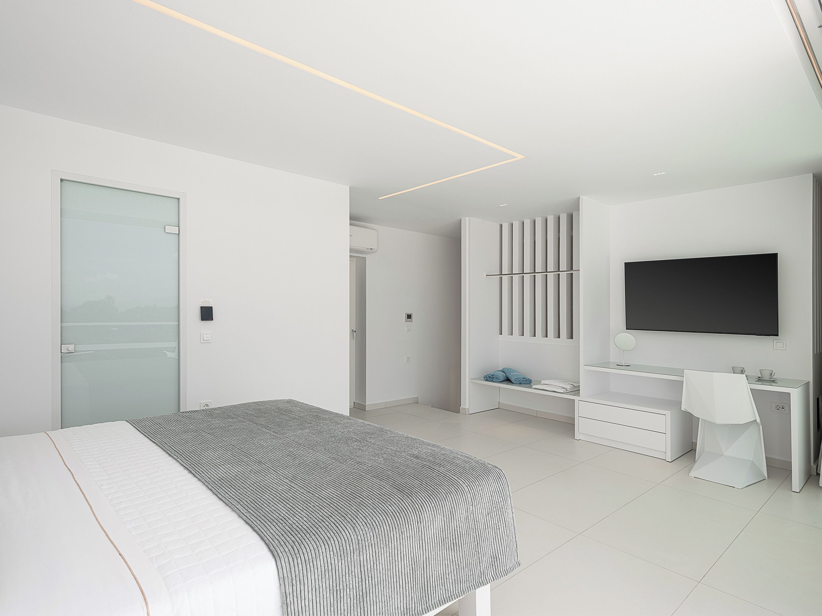 Ein modernes Schlafzimmer mit Bett, Fernseher, Schminktisch und begehbarem Kleiderschrank.