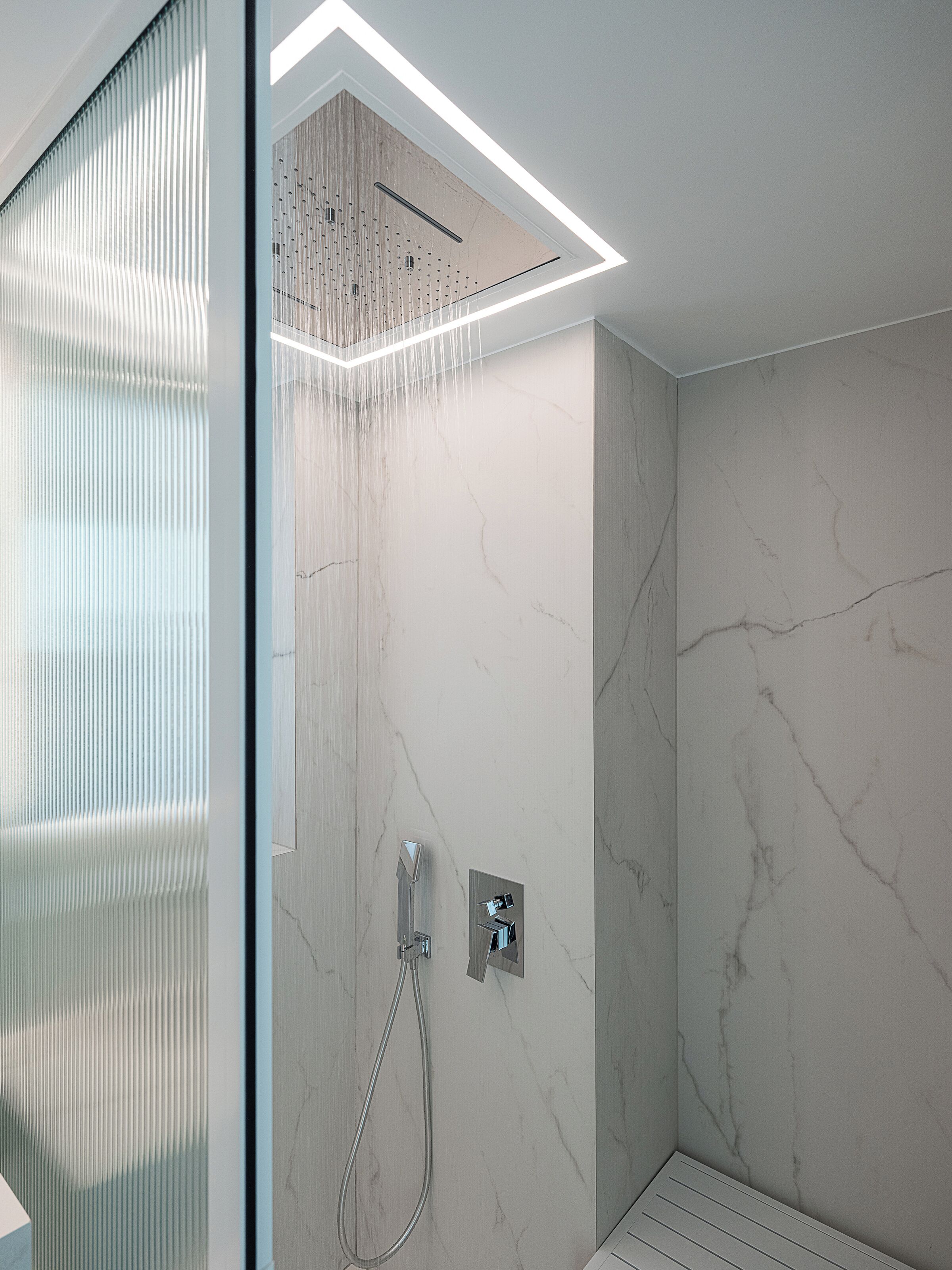 Een moderne douche met een glazen scheiding, een marmeren wand en een plafondlamp.