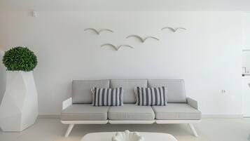 Een moderne woonkamer met een grijze bank, gestreepte kussens, een witte salontafel, een potplant en wanddecoraties van vogels.
