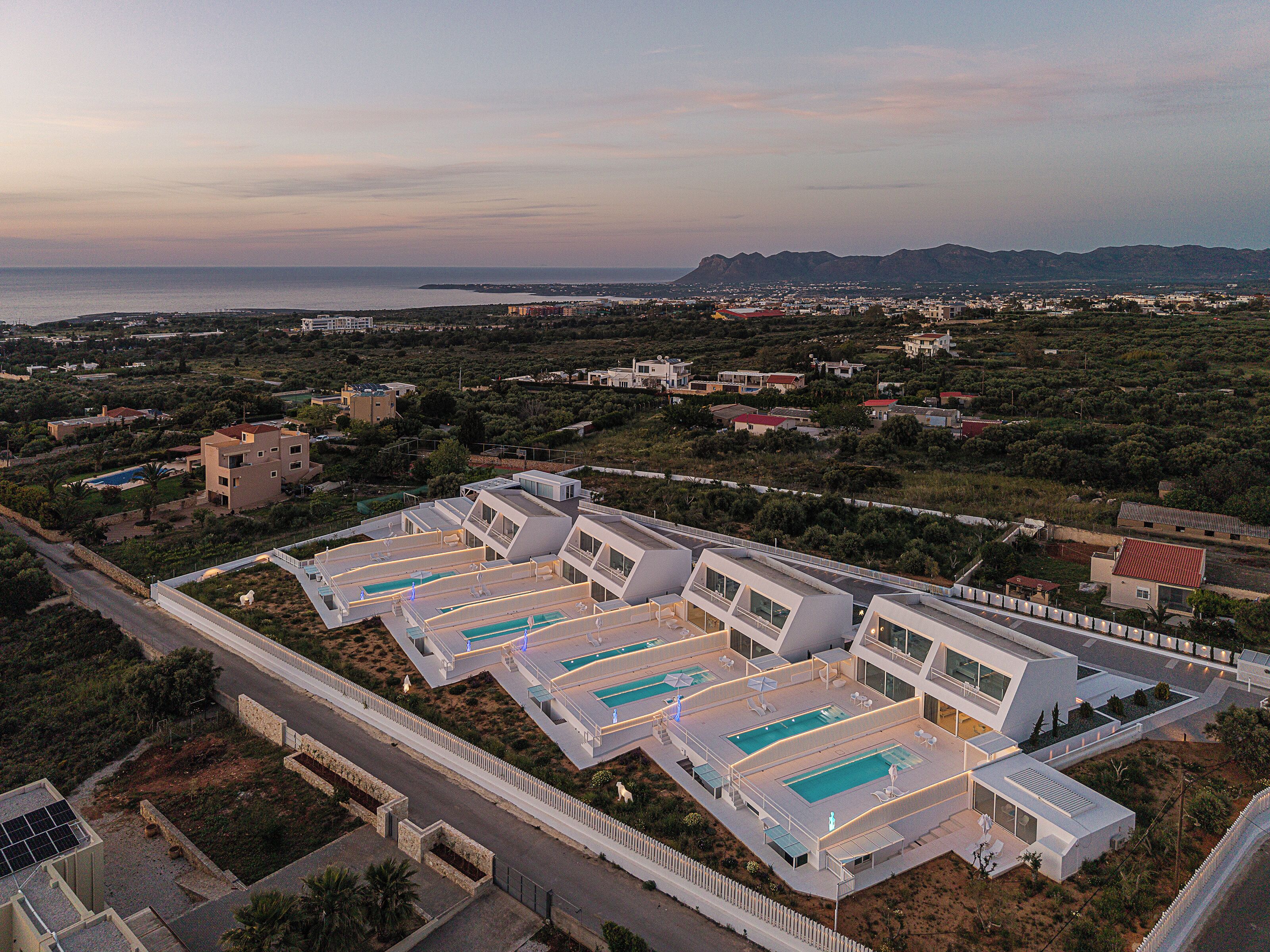 Un hôtel moderne doté de plusieurs piscines, offrant une vue sur la mer et surplombant un paysage vallonné.