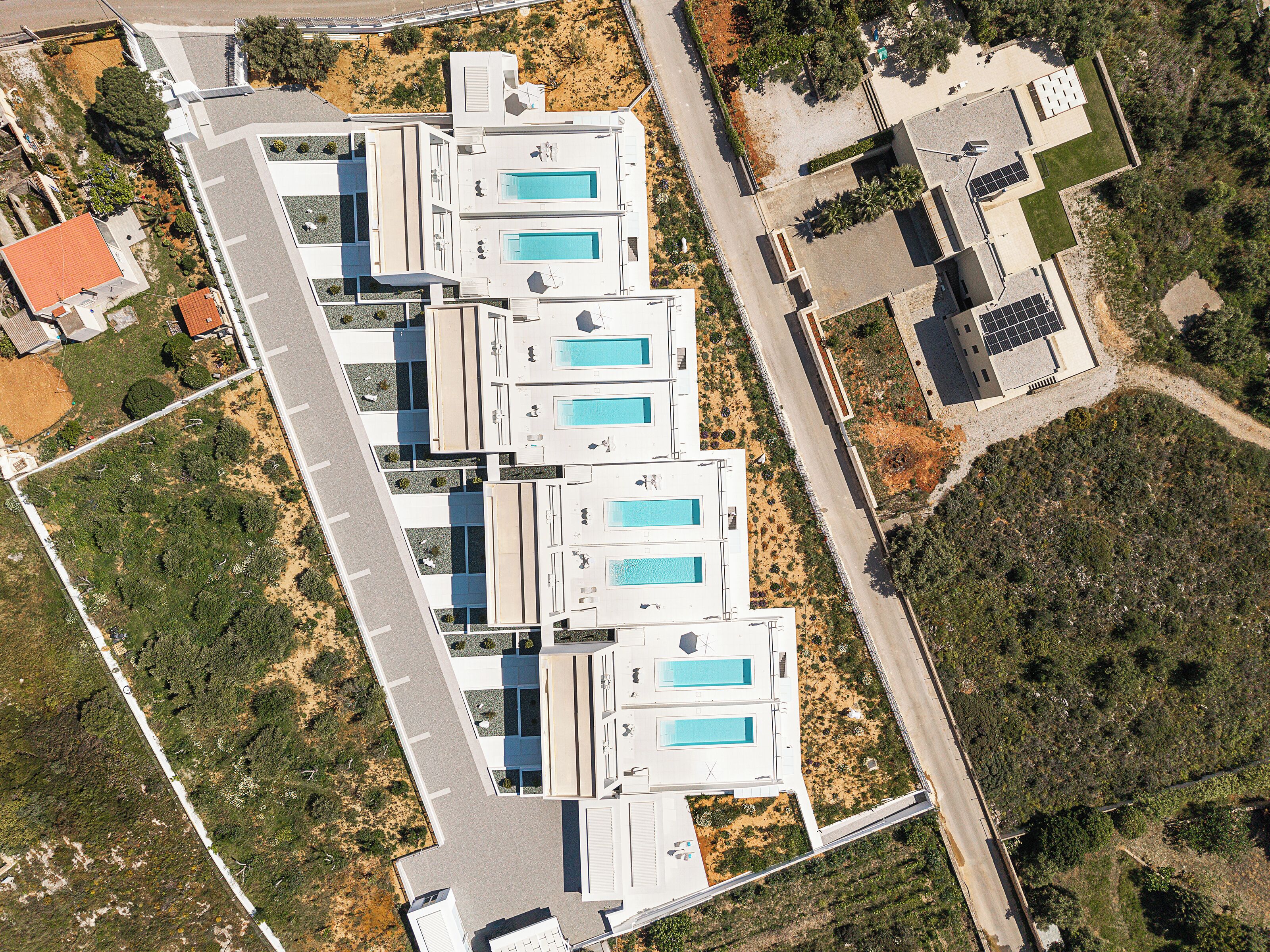A modern building with multiple swimming pools, a parking lot, and surrounding greenery.