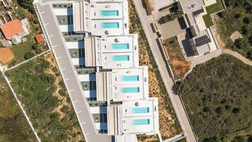 A modern building with multiple swimming pools, a parking lot, and surrounding greenery.
