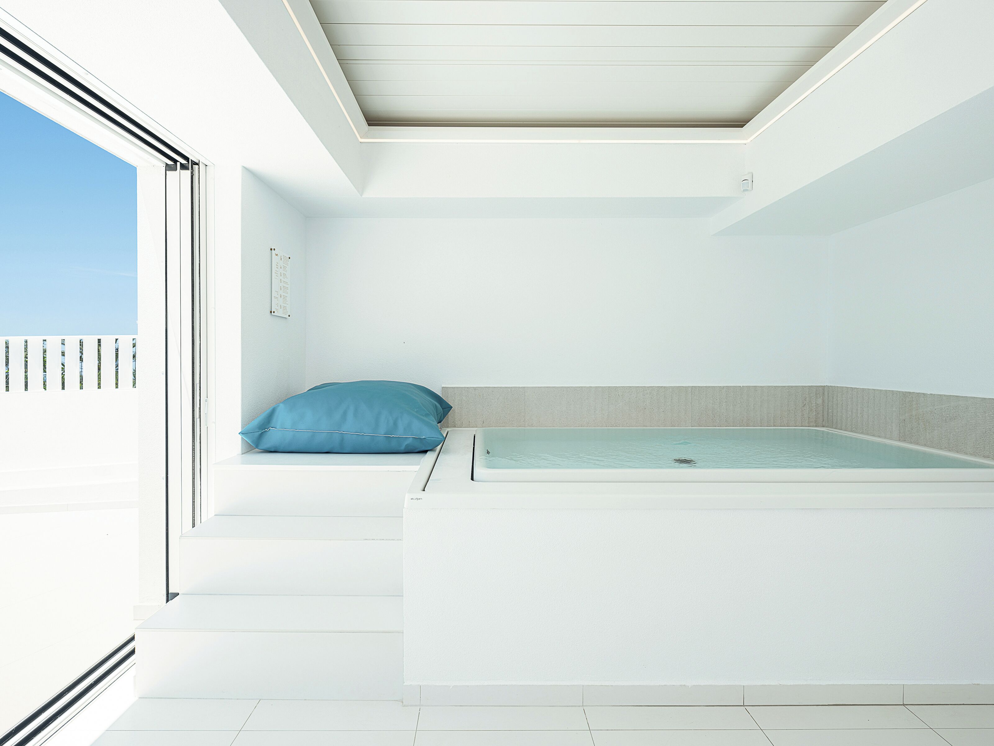 Una camera moderna con un lucernario, un letto con un cuscino blu e una piccola piscina.