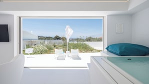 Een moderne slaapkamer met een groot raam, een bed, een witte stoel en een klein tafeltje.