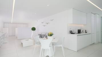 Un interior moderno y minimalista con comedor, mobiliario blanco y una cocina con armarios blancos.