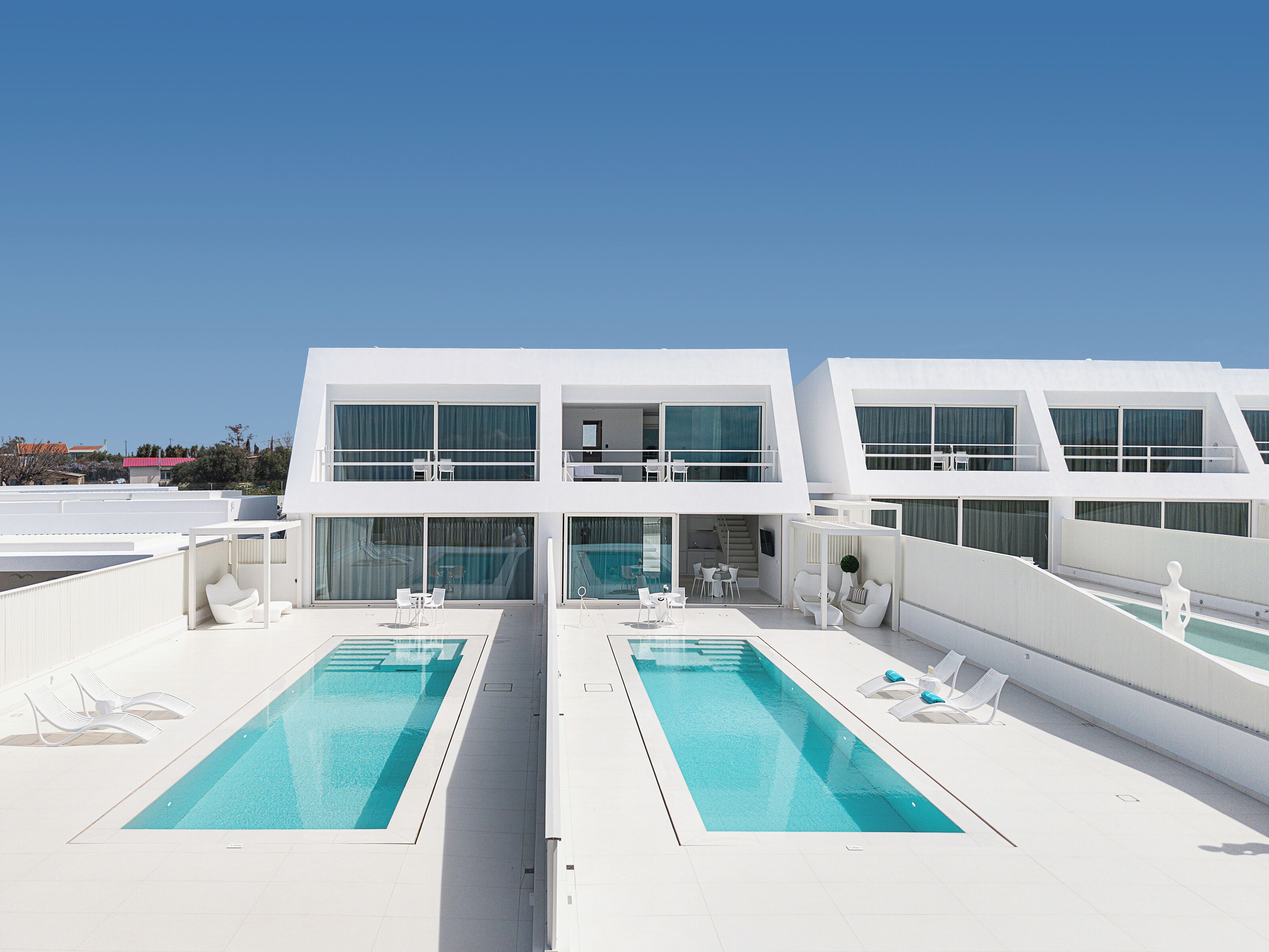 A modern cruise ship with two swimming pools, white lounge chairs, and a clear sky.