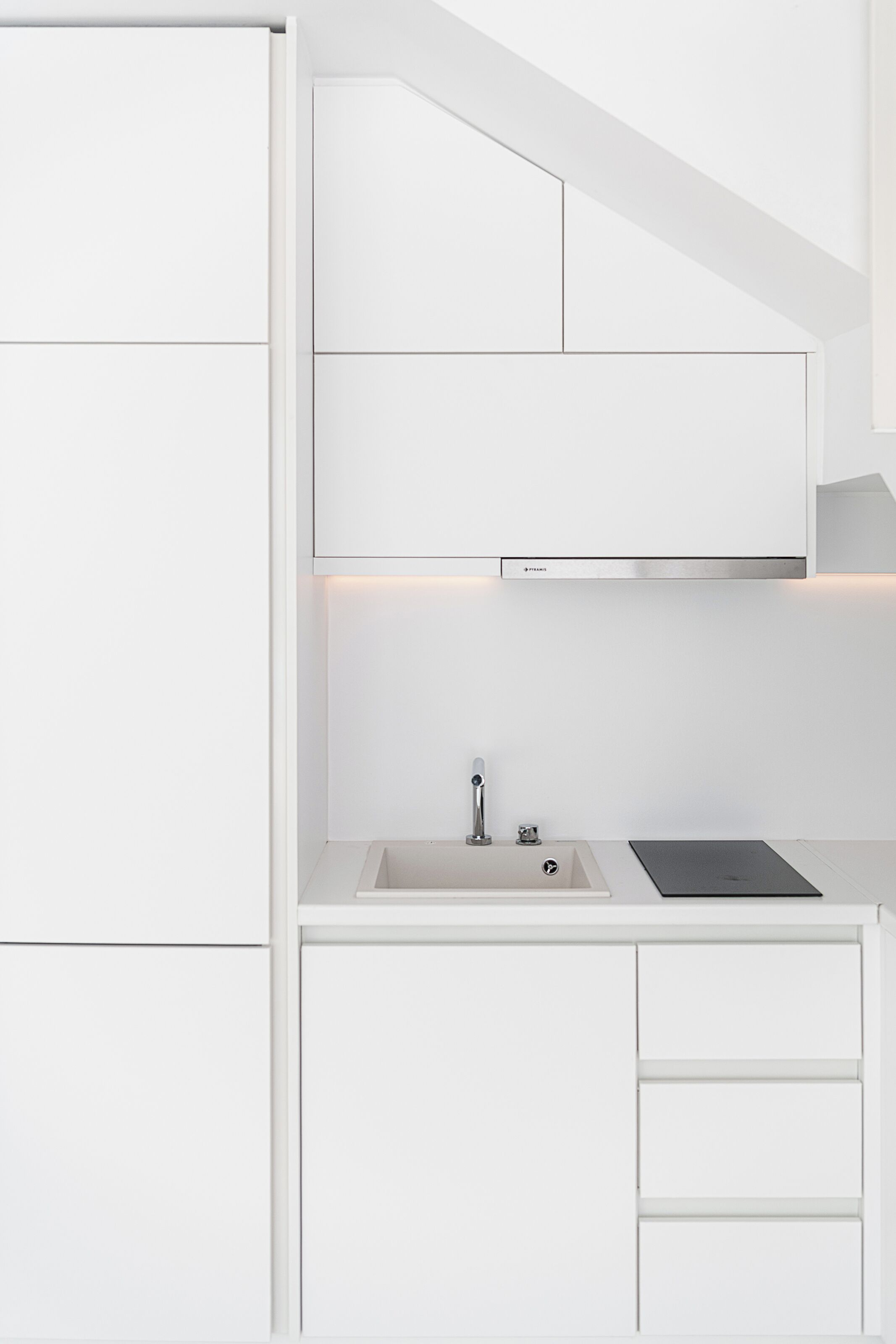 Une cuisine moderne avec des meubles blancs, une cuisinière encastrée et un évier.