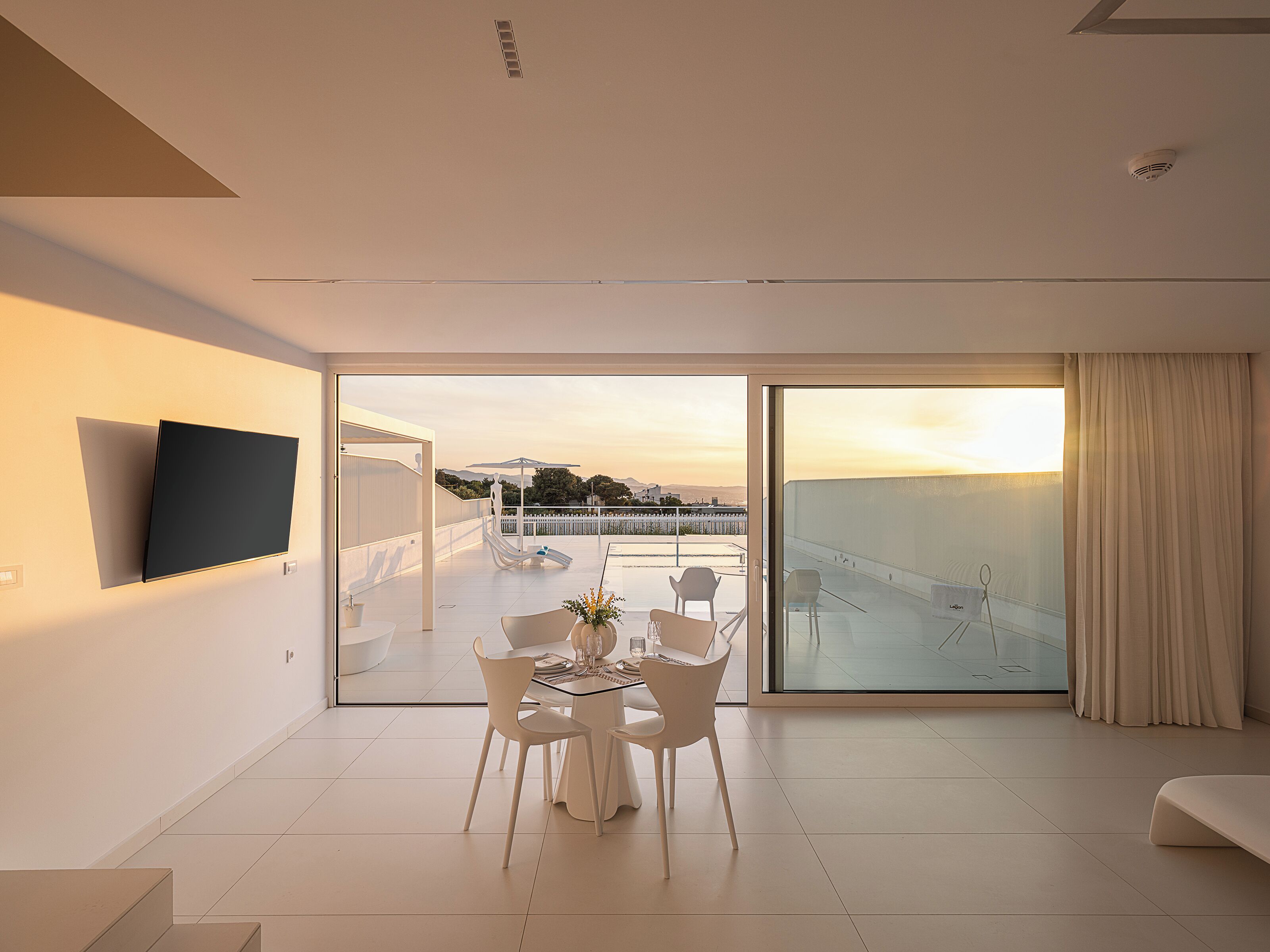 Ein modernes Wohnzimmer mit Flachbildfernseher, Essbereich mit Stühlen und Tisch sowie eine große Glasschiebetür, die zu einem Balkon mit Stadtblick führt.
