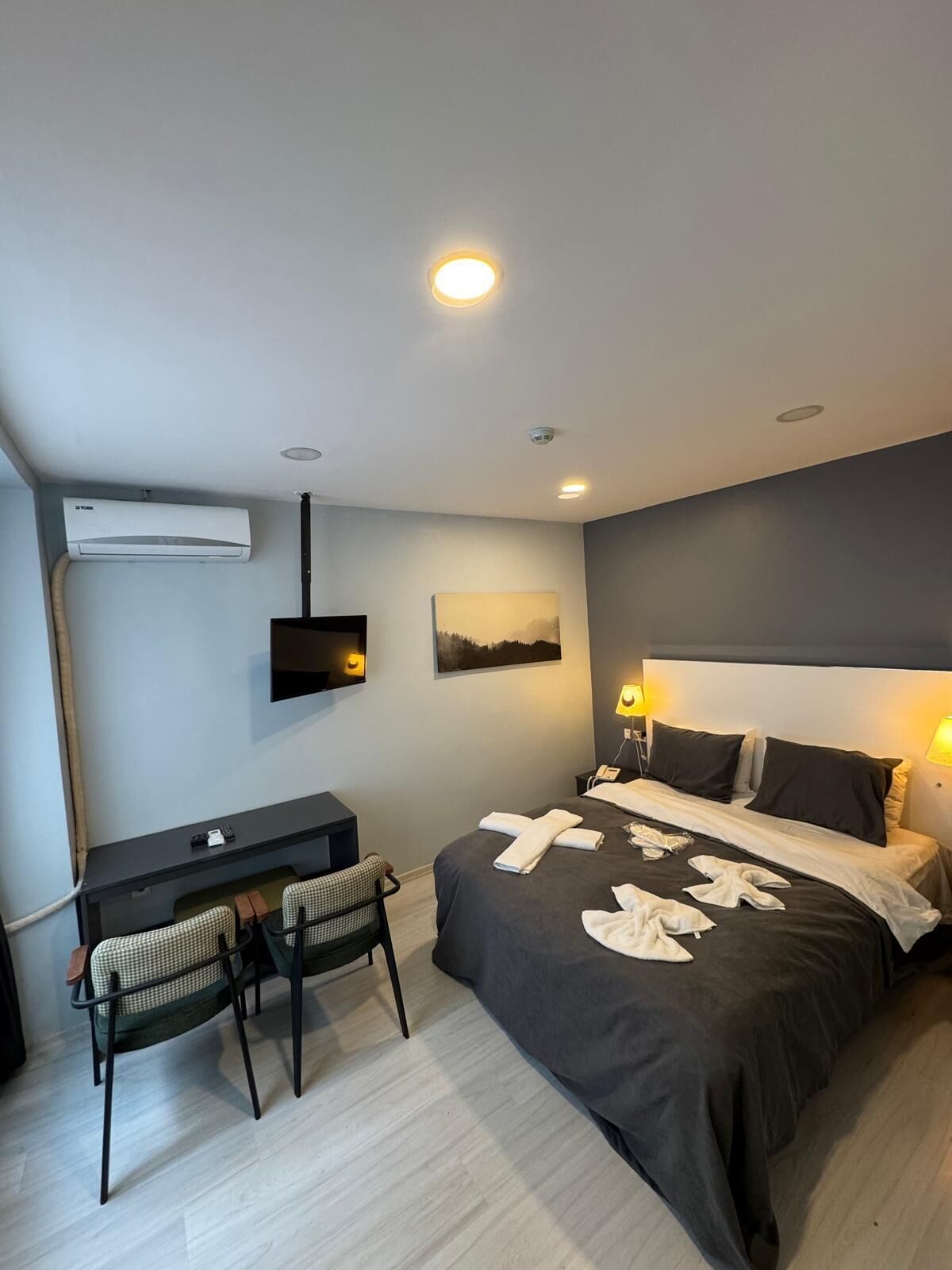 Une chambre d’hôtel comprenant un lit, des lampes de chevet, un bureau avec une chaise, un téléviseur à écran plat, un appareil de climatisation et un tableau au mur.