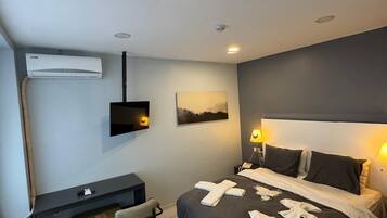 Une chambre d’hôtel comprenant un lit, des lampes de chevet, un bureau avec une chaise, un téléviseur à écran plat, un appareil de climatisation et un tableau au mur.