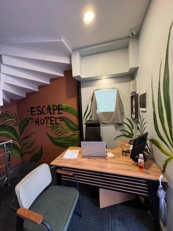 Une petite pièce moderne, équipée d’un bureau, d’une chaise, d’un ordinateur portable et d’un mur décoré d’une fresque représentant des plantes.