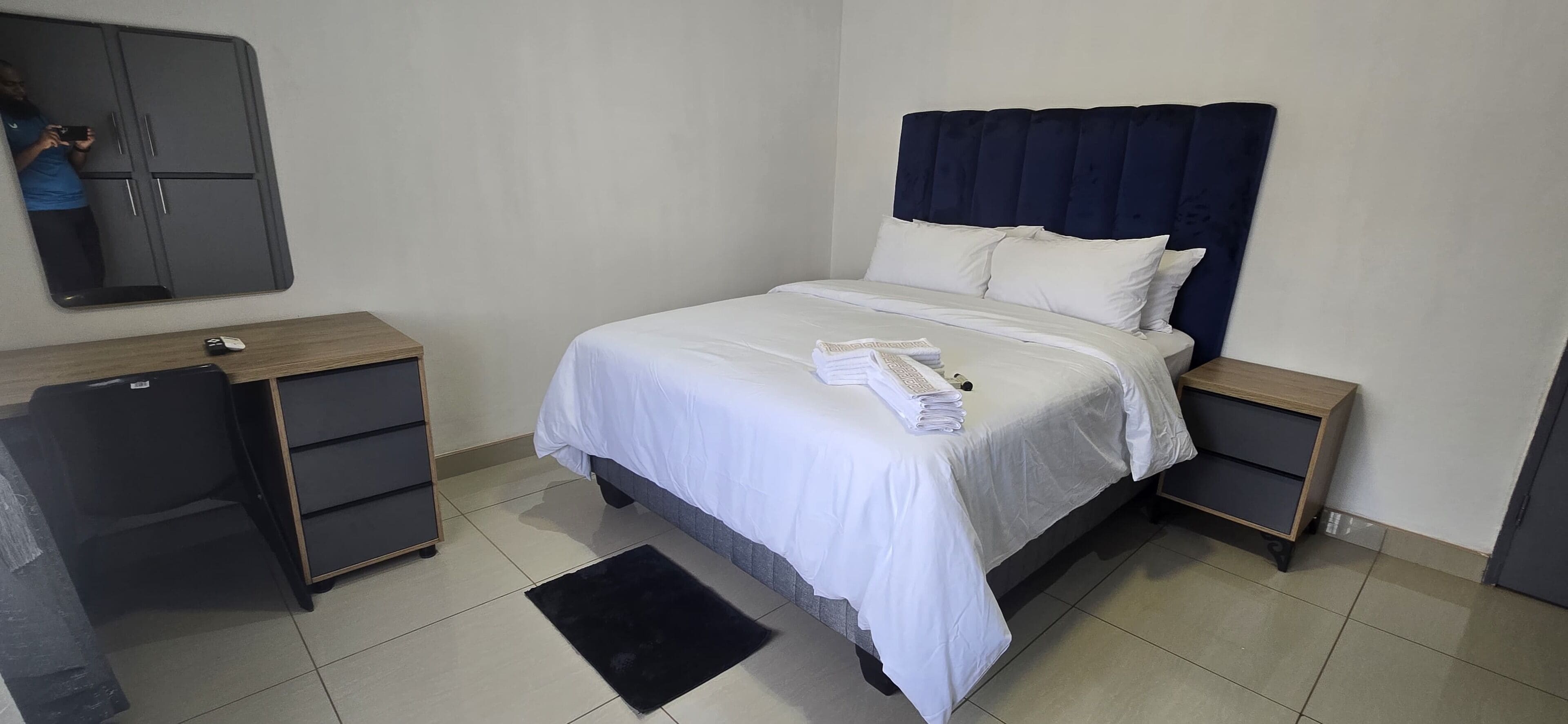 Ein ordentlich eingerichtetes Hotelzimmer mit einem Bett, Nachttischen, einem Kleiderschrank und einem Spiegel.