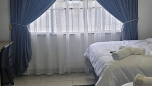 Et hotelværelse med to senge, et skrivebord og et vindue med blå gardiner.