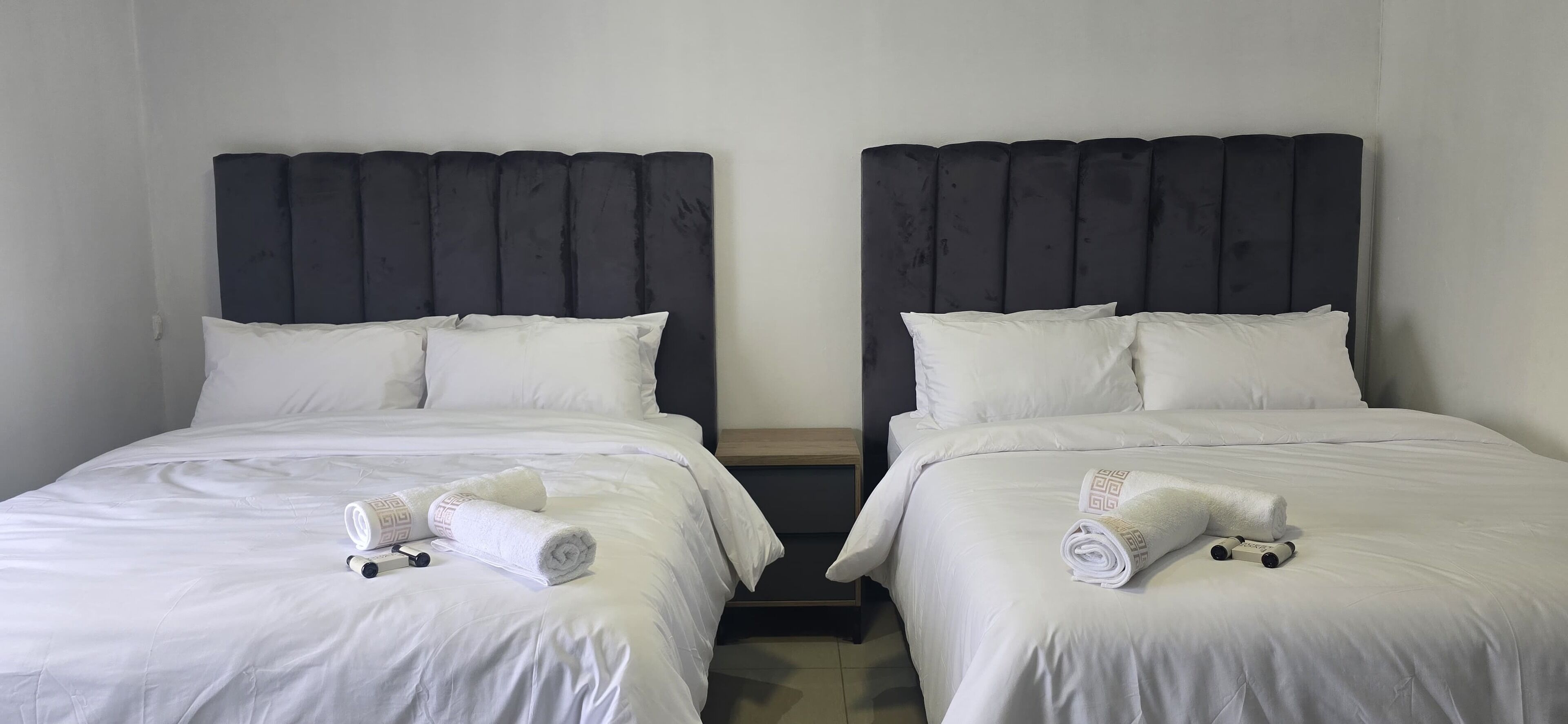 Two twin beds with dark headboards, white bedding, and rolled towels on each bed.