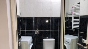 Een kleine badkamer met een toilet, een wasmachine en een afvalbak.
